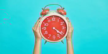 Old-fashioned coral colored alarm clock held against a bright blue background