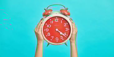 Old-fashioned coral colored alarm clock held against a bright blue background