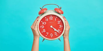 Old-fashioned coral colored alarm clock held against a bright blue background