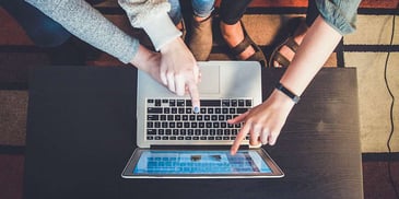 Top-down view of a laptop and three hands pointing at the screen