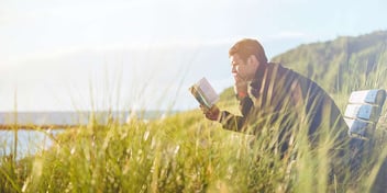Man reads a book by the beach surrounded by tall sea grass